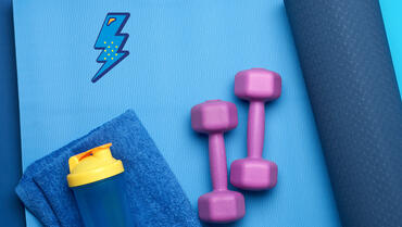 Une photo d'un tapis de yoga, de poids pour la musculation ainsi qu'une gourde d'eau et une serviette