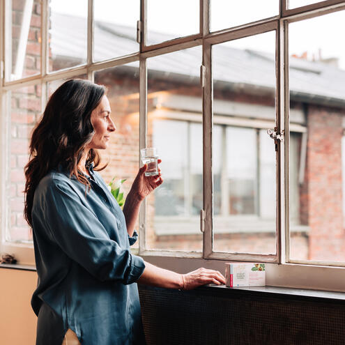 image représentant une femme avec un verre d'eau et qui regarde par la fenêtre