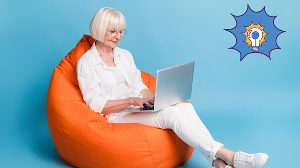 Personne âgé sur un pouf en train de taper sur un ordinateur portable posé sur ses genoux