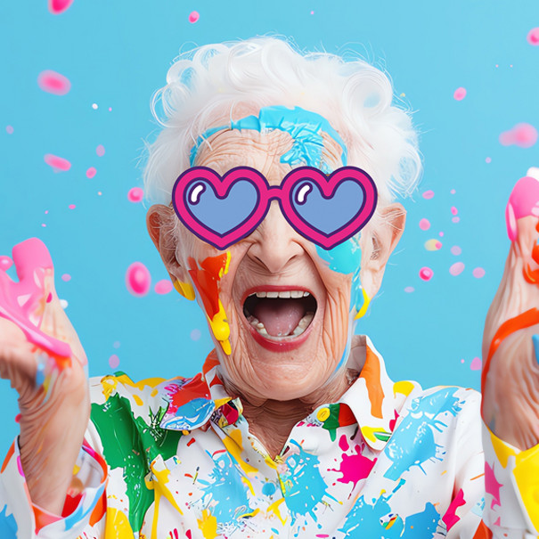 Personne âgé souriante avec des lunettes un cœur dessiné sur le visage et levant des mains pleines de peinture