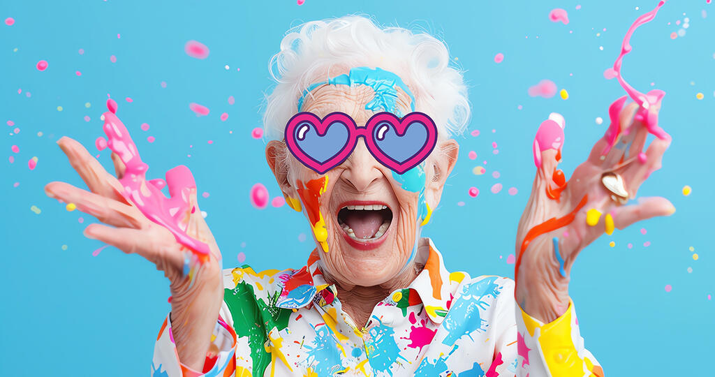 Personne âgé souriante avec des lunettes un cœur dessiné sur le visage et levant des mains pleines de peinture